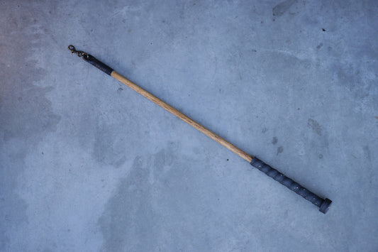 Wooden cat wand with black leather on a gray concrete surface